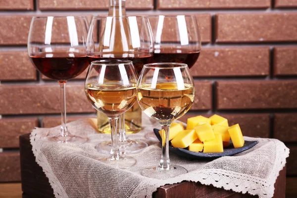 Glasses of wine and cheese on table on brick wall background — Stock Photo, Image