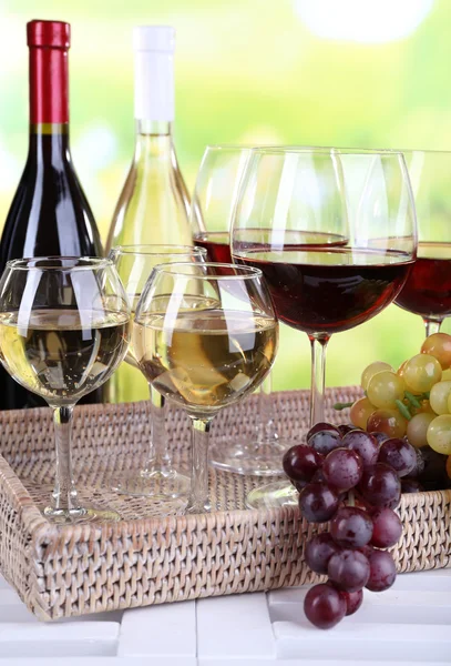 Flaschen und Gläser mit Wein und reifen Trauben auf dem Tisch vor natürlichem Hintergrund — Stockfoto