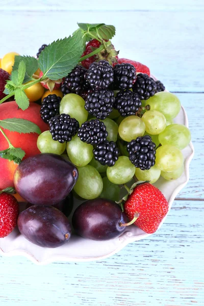 Diferentes bayas y frutas en plato sobre tabla de madera de primer plano —  Fotos de Stock