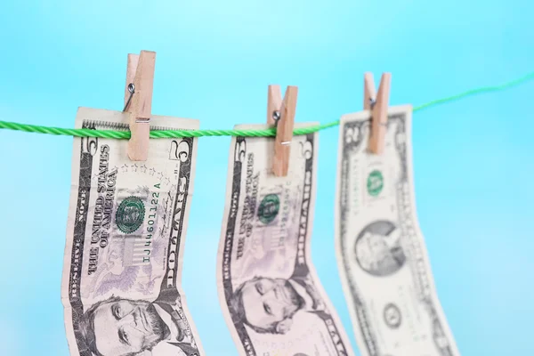 Dollar bills hanging on rope attached with clothes pins. Money-laundering concept. On bright background. — Stock Photo, Image