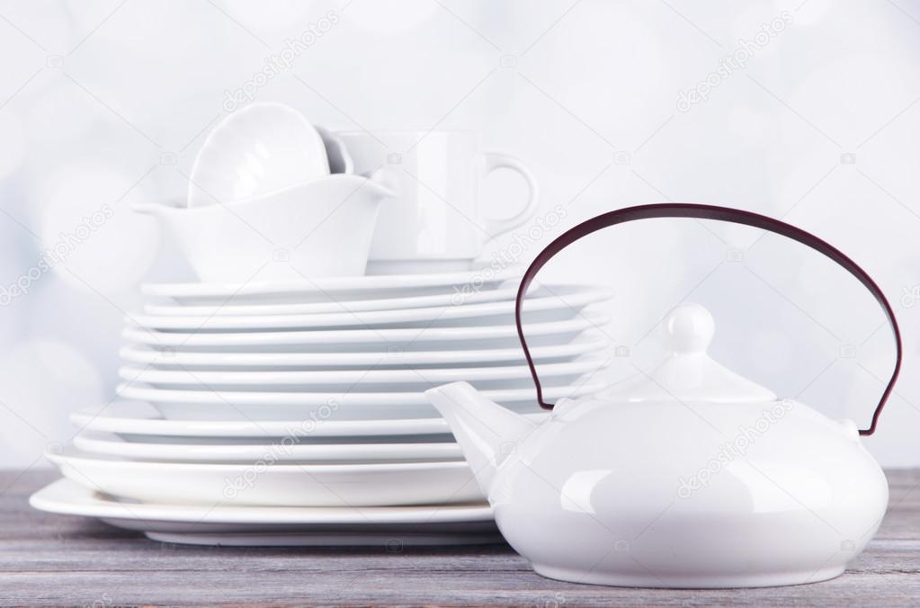 White crockery and kitchen utensils, on wooden table, on light background