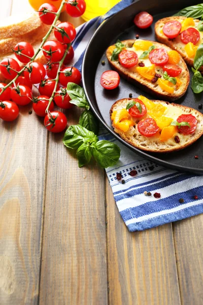 Tasty bruschetta with tomatoes on pan, on old wooden table — Stock Photo, Image