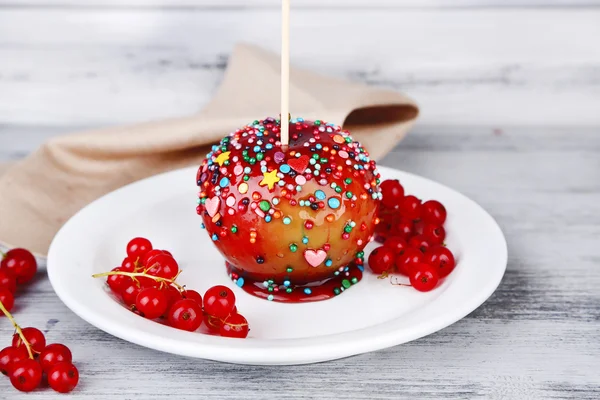 Süßer Karamell-Apfel am Stiel mit Beeren, auf Holztisch — Stockfoto