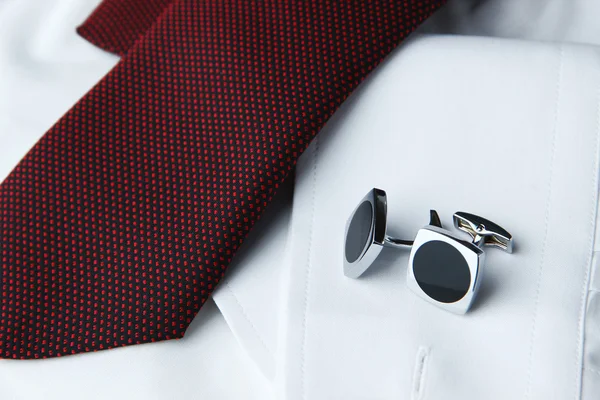 A pair of cuff links on a sleeve of the white shirt and a cravat near it — Stock Photo, Image