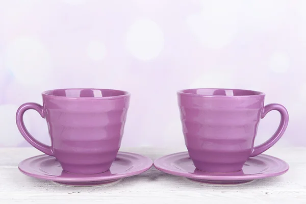 Purple cups and saucers on table on bright background — Stock Photo, Image