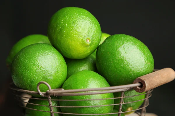 Freschi e succosi lime in cesto su tavolo di legno, su sfondo scuro — Foto Stock