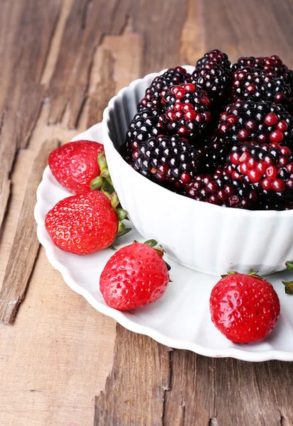 Cuenco de moras y plato de fresas sobre fondo de madera — Foto de Stock