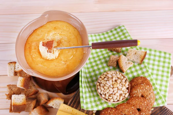 Fondue, biscuits, slices of cheese and rusks on cutting board on napkin on wooden background — Stock Photo, Image