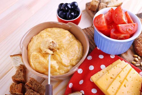 Fondue, tomatoes, biscuits, slices of cheese and rusks on cutting board on polka dot napkin on wooden background