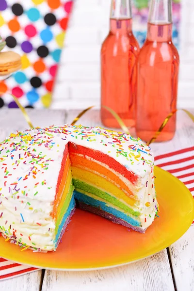 Köstlicher Regenbogenkuchen auf Teller auf Tisch vor hellem Hintergrund — Stockfoto