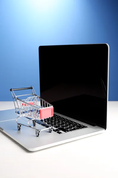 Shopping cart on laptop on table, on blue background — Stock Photo, Image