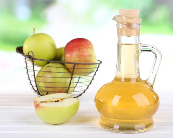 Vinagre de sidra de manzana en botella de vidrio y manzanas frescas maduras, sobre mesa de madera, sobre fondo natural — Foto de Stock