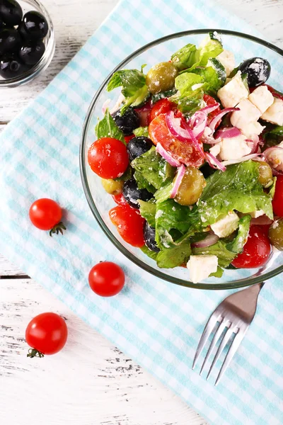 Glass bowl of Greek salad served on napkin on wooden background — Stock Photo, Image