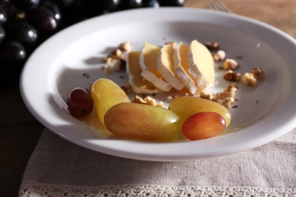Lezzetli üzüm ve ahşap masa üzerinde plaka üzerinde peynir — Stok fotoğraf