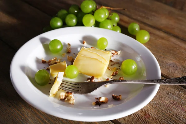 Tasty grape and cheese on plate, on wooden table — Stock Photo, Image