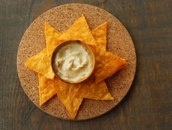 Nachos saborosos e tigela com molho a bordo, em fundo de madeira — Fotografia de Stock