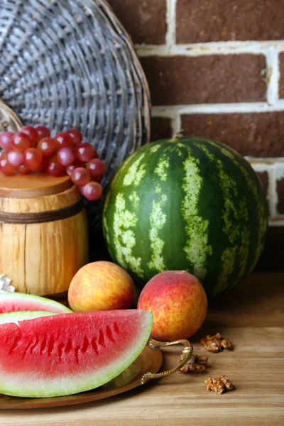 Samenstelling van rijp watermeloen, fruit en houten vat op kleur houten tafel, op bakstenen achtergrond — Stockfoto