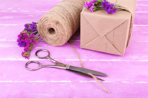 Beautiful gift with flowers and decorative rope, on old wooden background — Stock Photo, Image