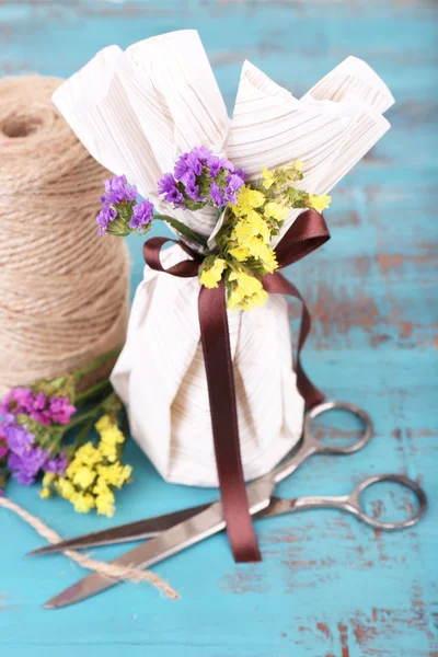 Bellissimo regalo con fiori e corda decorativa, su sfondo vecchio in legno — Foto Stock