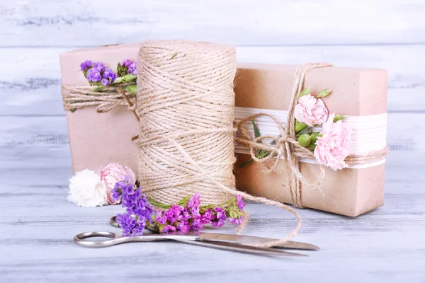 Prachtige geschenken met bloemen en decoratieve touw, op oude houten achtergrond — Stockfoto