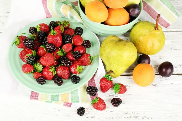 Ripe berries on plate and fruits on table close up — Stock Photo, Image