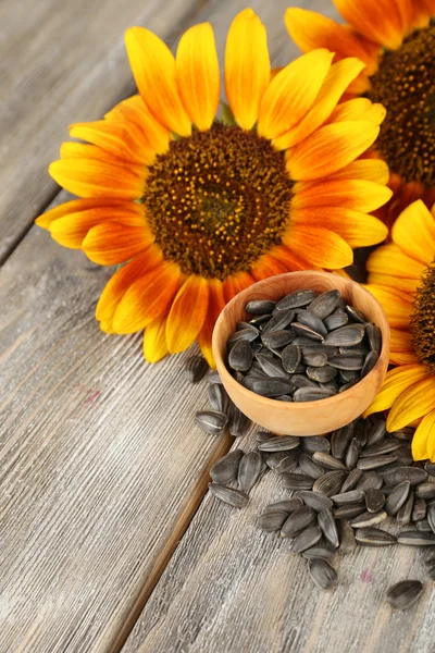 Sunflowers and seeds in bowl on wooden background — Stock Photo, Image