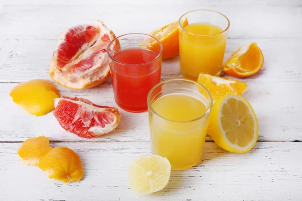 Different sliced citrus fruits and glasses of juice on wooden table — Stock Photo, Image