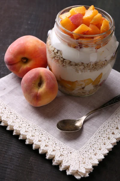 Gezond ontbijt - yoghurt met vers perzik en muesli geserveerd in glazen pot, op houten achtergrond — Stockfoto