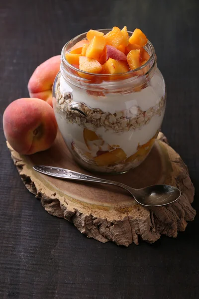 Healthy breakfast - yogurt with  fresh peach and muesli served in glass jar, on wooden background — Stock Photo, Image