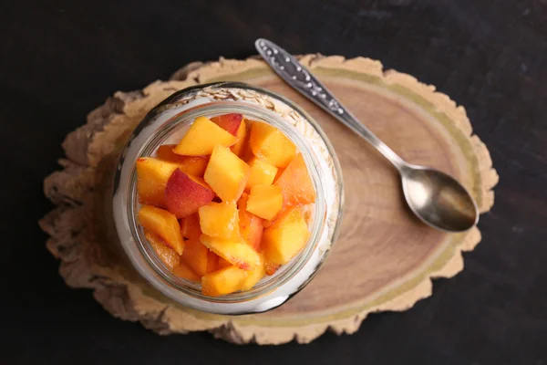 Colazione sana - yogurt con pesca fresca e muesli servito in barattolo di vetro, su sfondo di legno — Foto Stock