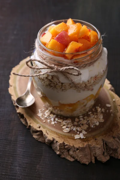 Здоровий сніданок - йогурт зі свіжим персиком та мюслі, поданий у скляній банці, на дерев'яному фоні — стокове фото