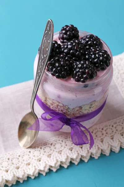 Здоровый завтрак - йогурт с ежевикой и мюсли подается в стеклянной банке, на цветном деревянном фоне — стоковое фото