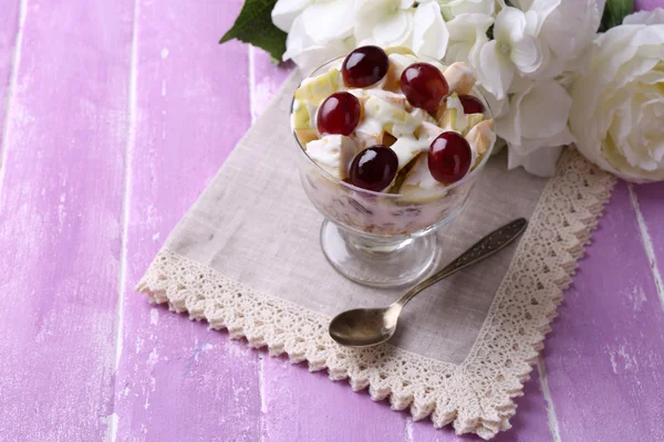 Gesundes Frühstück - Joghurt mit frischen Trauben- und Apfelscheiben und Müsli in Glasschüssel serviert, auf farbigem Holzgrund — Stockfoto