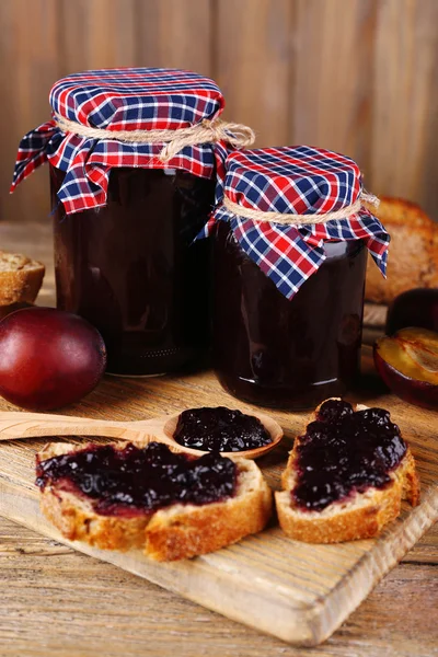 Tasty plum jam in jars and plums on wooden table — Stock Photo, Image