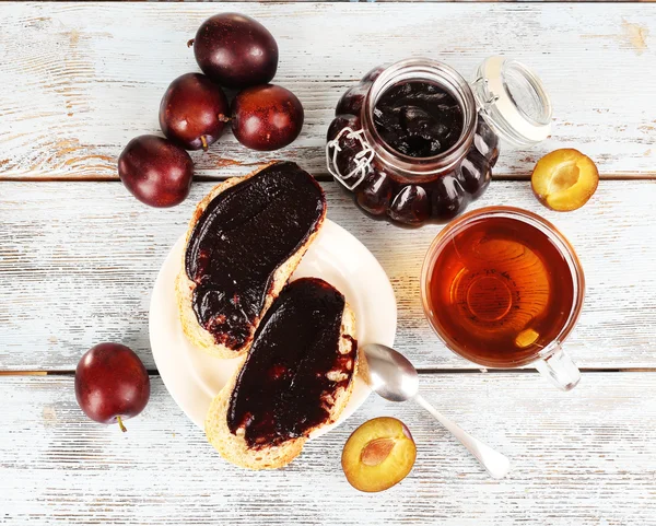 Bread with plum jam and tea on wooden table — Stock Photo, Image