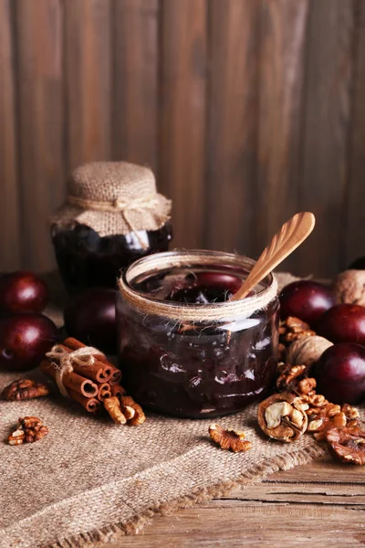 Sabrosa mermelada de ciruela en tarros y ciruelas sobre mesa de madera sobre fondo de madera — Foto de Stock