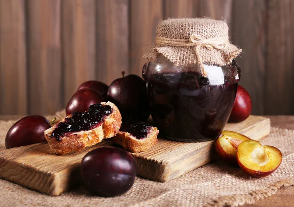 Smakelijke pruim jam in kruik en pruimen op houten tafel close-up — Stockfoto