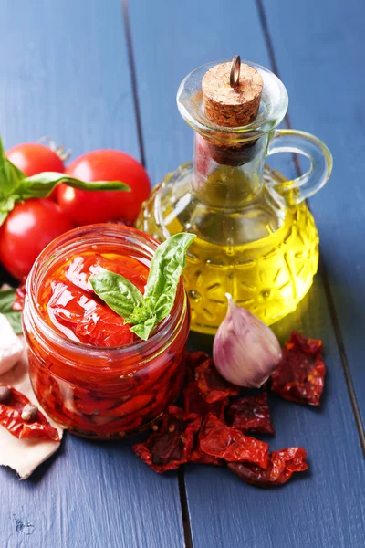 Zongedroogde tomaten in glazen pot, olijfolie in glazen fles en feta kaas op een houten achtergrond kleur — Stockfoto
