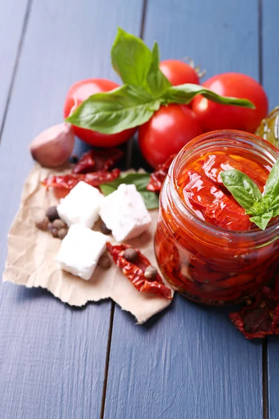 Tomates secos ao sol em jarra de vidro, azeite em garrafa de vidro e queijo feta em fundo de madeira de cor — Fotografia de Stock