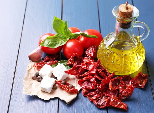 Tomates secados al sol en frasco de vidrio, aceite de oliva en botella de vidrio y queso feta sobre fondo de madera de color —  Fotos de Stock