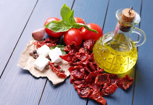 Tomates secados al sol en frasco de vidrio, aceite de oliva en botella de vidrio y queso feta sobre fondo de madera de color — Foto de Stock