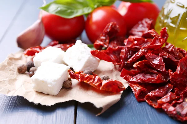 Tomates secados al sol en frasco de vidrio, aceite de oliva en botella de vidrio y queso feta sobre fondo de madera de color —  Fotos de Stock