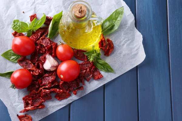 Sun dried tomatoes in glass jar, olive oil in glass bottle, basil leaves on color wooden background — Stock Photo, Image