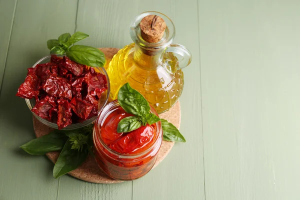 Pomodori secchi in vaso di vetro, olio d'oliva in bottiglia di vetro, foglie di basilico su fondo di legno — Foto Stock