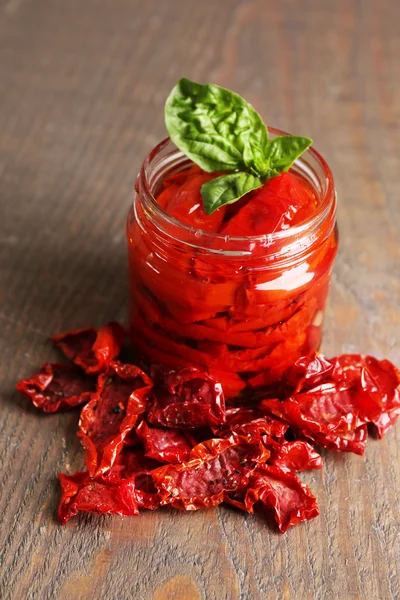 Zon gedroogde tomaten in glazen pot, Basilicum bladeren op houten achtergrond — Stockfoto