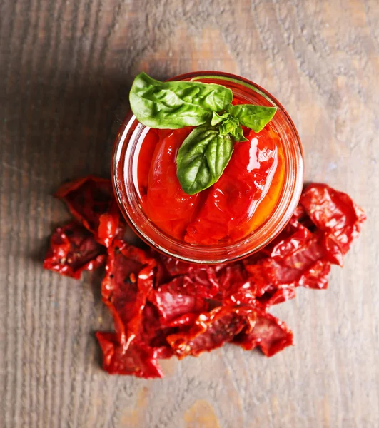 Sonnengetrocknete Tomaten im Glas, Basilikumblätter auf Holzgrund — Stockfoto