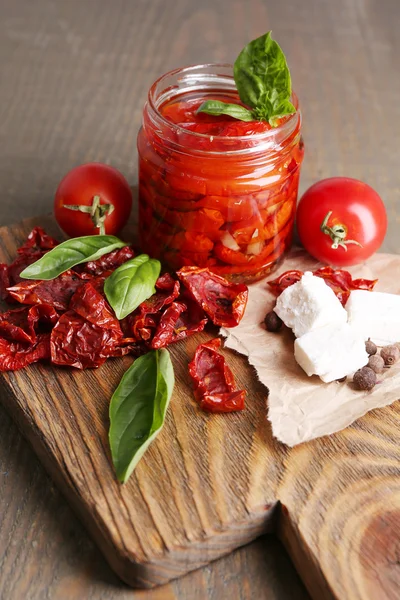 Sušenými rajčaty do sklenice, listy bazalky a sýr feta na prkénko, na dřevěné pozadí — Stock fotografie