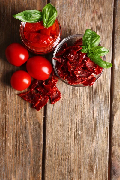 Sun dried tomatoes in glass jar, basil leaves on wooden background — Stock Photo, Image