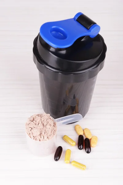 Whey protein powder in scoop with vitamins and plastic shaker on wooden background — Stock Photo, Image