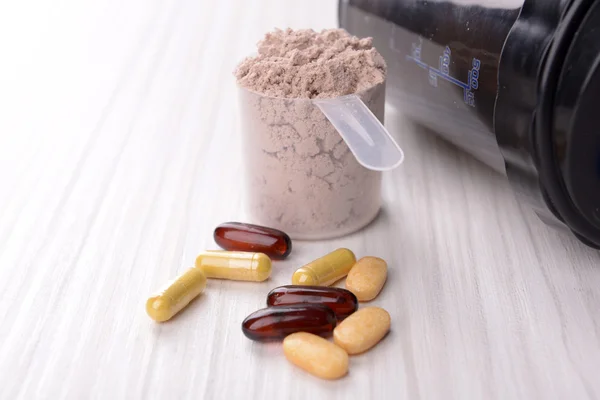 Whey protein powder in scoop with vitamins and plastic shaker on wooden background — Stock Photo, Image